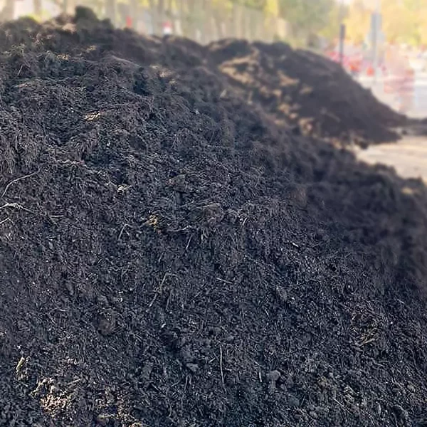Montón de compost oscuro y húmedo, con textura rica en materia orgánica, utilizado para fertilizar suelos en huertos y jardines.
